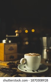 A Cup Of Coffee, Capuccino. A Nice Composition With A Coffee Grinder, An Espresso Maker And Some Chocolate. Restaurant And Coffee Shop. Nice Creamy Bokeh.