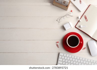Cup of coffee with computer keyboard, notebook and earphones on white wooden background