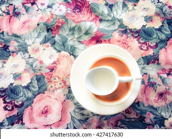 A Cup Of Coffee With Cream On The Flower Table Cloth