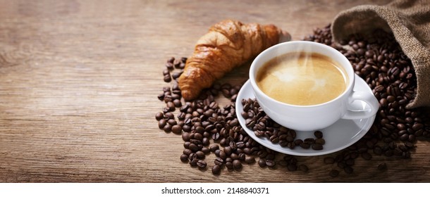 Cup Of Coffee, Croissant And Coffee Beans On A Wooden Table