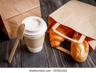 cup coffee and croissant in paper bag on wooden background