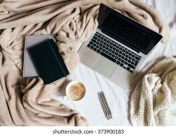 A cup of coffee, diary and address book with the laptop on the bed with a beige plaid