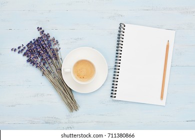 Cup of coffee, empty notebook and lavender flower on blue table top view. Woman working desk. Cozy breakfast. Flat lay style.