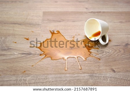 A cup of coffee fell on laminate, coffee spilled on floor. Focus on the puddle.