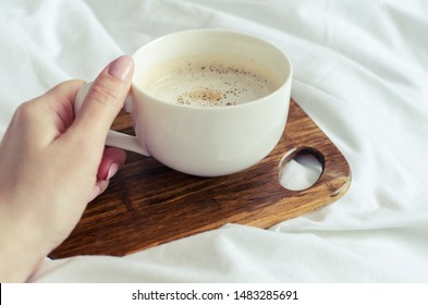 A Cup Of Coffee In Female Hand In Bed On A White Blanket. Moman Enjoying Comfort At Cozy Home Atmosphere. Good Morning. POV.