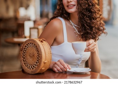 Cup of coffee in female hands. Happy smiling curly brunette woman drinking cappuccino in street cafe in European city. Soft focus
 - Powered by Shutterstock