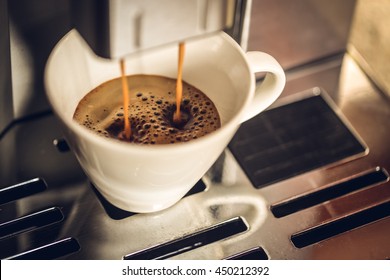 A cup of coffee filled with fresh cooked coffee in a coffee machine. Filtered with soft pastel colors.