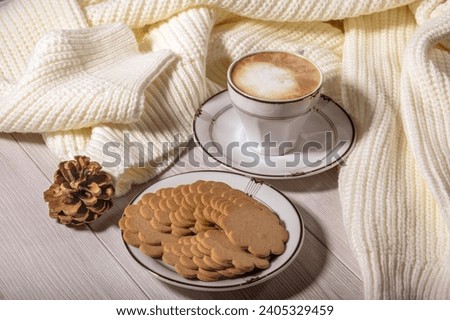 Cup of coffee, ginger cookies and warm white sweater on a white table. Cozy winter still life.
