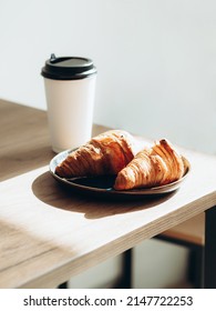 Cup Of Coffee To Go In White Paper Cup And Croissants In Sunlight On Wood Table. Morning Coffee In Cafe Place For Text.