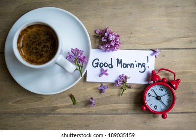 Cup Of Coffee, Good Morning Note And Lilac Flower On The Wooden Table