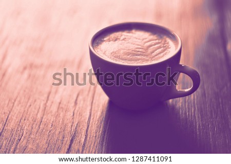 A cup of coffee with heart pattern in a white cup on wooden background. concept, duotone toning