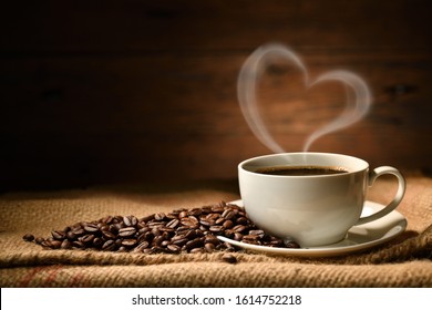 Cup of coffee with heart shape smoke and coffee beans on burlap sack on old wooden background