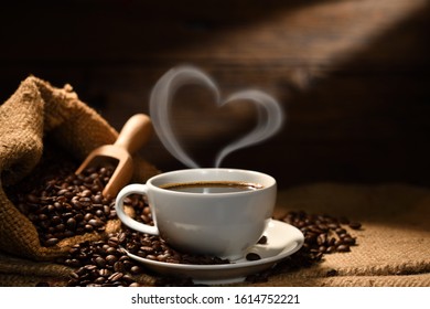 Cup of coffee with heart shape smoke and coffee beans on burlap sack on old wooden background