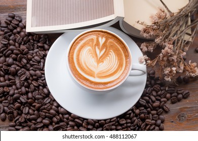 a cup of coffee with heart shape symbol on a wooden and bean, A cup of coffee with heart shape on dry flower and book