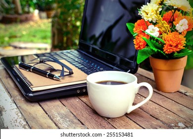 Cup Of Coffee And Laptop On Wooden Table With Flower And Notebook In The Garden, Vintage Style