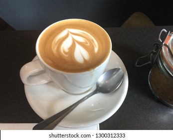A cup of coffee latte with a spoon on a dark table