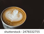 A cup of coffee with a leaf design on top. The coffee is hot and steaming. The cup is white and black with a Starbucks logo