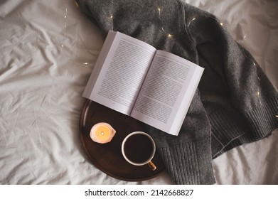 Cup of coffee with leopard print staying on wooden tray with scented burning candle and open paper book on knitted textile in bed at home. Good morning. Breakfast time. Cozy hygge atmosphere. Top view - Powered by Shutterstock