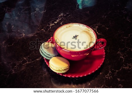 Cup of coffee with macaroon on table. Red cup of cappuccino and saucer with macaroon cookie on wooden desk.