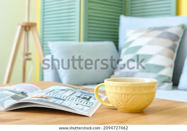 Cup of coffee and magazine on table in living\
room, closeup