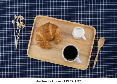 A Cup Of Coffee, Milk And Croissant With White Flower And Wooden Spoon On Dark Blue Table Cloth 