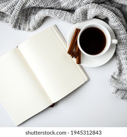 Cup Of Coffee With Notebook Cinnamon Sticks And Anise Star On White Background. Sweater Around. Winter Morning Routine. Coffee Break. Copy Space. Top View. Breakfast. Flat Lay