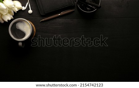 Cup of coffee, notebook, earphone and tulips on black wooden table. Flat lay, copy space.