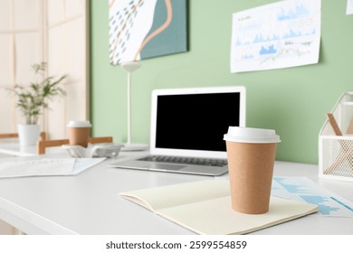 Cup of coffee with notebook on table in office, closeup