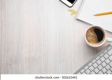 Cup of coffee with office tools on light wooden background