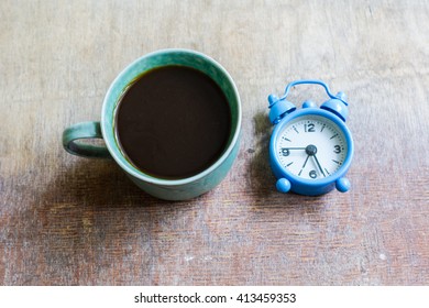 Cup of coffee and old-styled clock on rustic wooden table