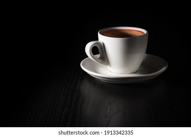 Cup of coffee on black wood table. White porcelain cup on saucer. Copy space