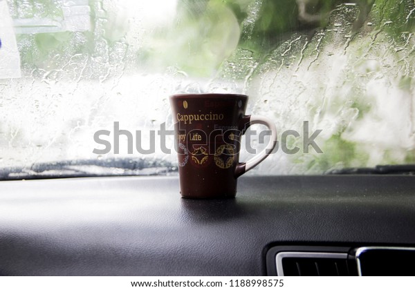 A\
 cup of coffee on the dashboard of a car on a rainy\
day