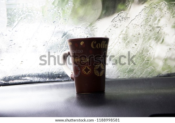 A\
 cup of coffee on the dashboard of a car on a rainy\
day