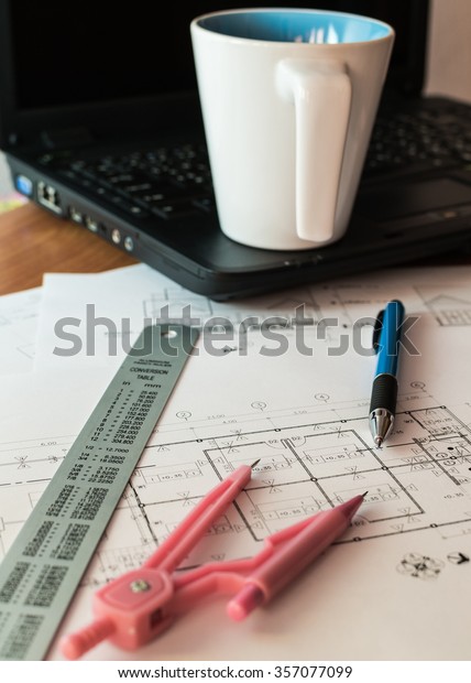 Cup of coffee on laptop with construction\
plans, pen and drawing\
materials