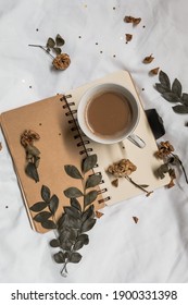 A Cup Of Coffee On A Notebook And White Sheet With Dried Leaves And Flowers.Aesthetic Concept