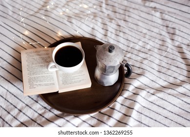 Cup Of Coffee On Open Book With Coffee Maker In Room Closeup. Bedtime. Good Morning. 