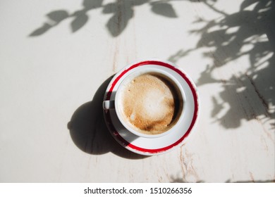 Cup Of Coffee On A Plate, With A Shadow From The Sun, On A Table In A Street Cafe  Natural Lighting