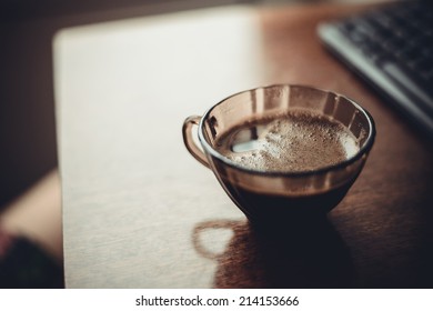 cup of coffee on  table near  keyboard in  morning