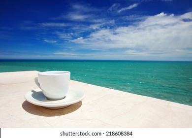 A cup of coffee on table with sea at the background