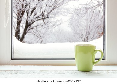 Cup Of Coffee On The Window Sill. In The Background, A Beautiful Winter Landscape In Snow. Cozy Home Concept