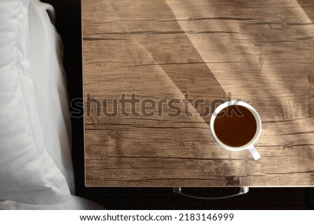 Cup of coffee on wooden night stand near bed in morning, top view. Space for text
