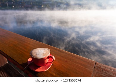 A Cup Of Coffee On Wooden Table With Steam Over Lake At Rakthai Village, Mae Hong Son, Thailand