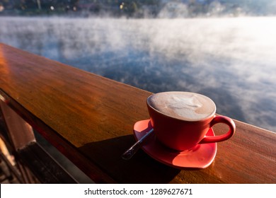 A Cup Of Coffee On Wooden Table With Steam Over Lake At Rakthai Village, Mae Hong Son, Thailand