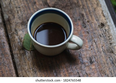 A Cup Of Coffee On A Wooden Table Next To A Single Green Leaf