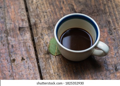 A Cup Of Coffee On A Wooden Table Next To A Single Green Leaf