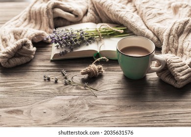 A Cup Of Coffee On A Wooden Table, An Open Book And A Warm Sweater On The Background Of A Bouquet Of Lavender Flowers. Still Life Concept. Cozy Morning.