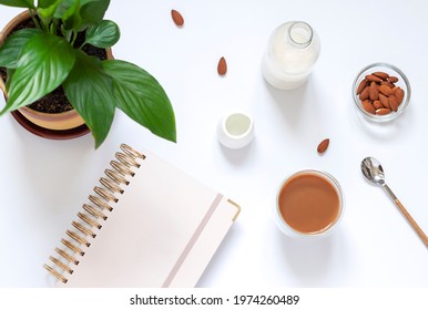 A Cup Of Coffee With Organic Almond Milk On The White Table With A Notepad. Dairy Free Vegan Coffee Break Concept. Top View	