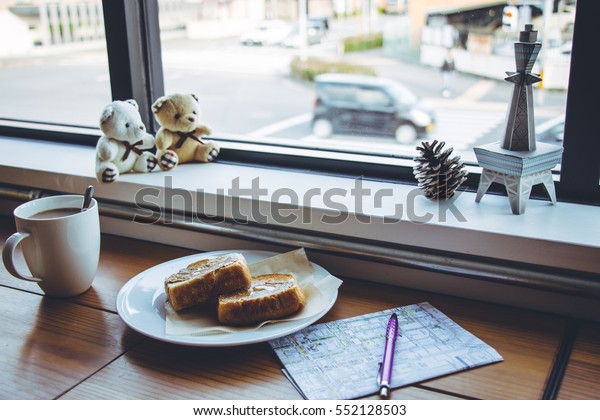 cup of coffee and Peanut butter bread on wooden\
bar at glass window, Outfit of travel planner with Kyoto map and\
pen.Travel concept