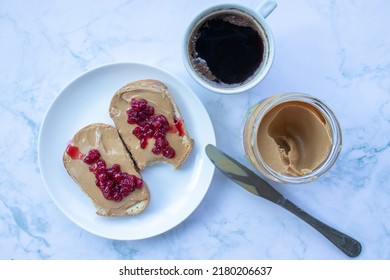 Cup Of Coffee, Peanut Butter Jelly Toasts, Knife And Glass Jar On White Marble Table Background In The Kitchen. Making Healthy Breakfast Process. Flat Lay, Top View, Copy Space