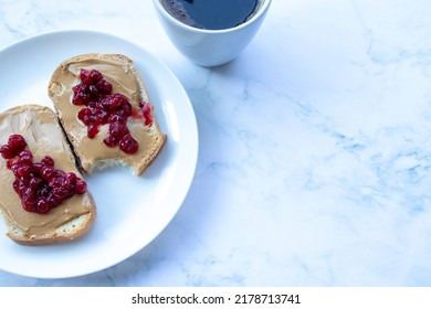 Cup Of Coffee And Peanut Butter Toasts With Berry Jelly On White Marble Table Background In The Kitchen. Making Heakthy Breakfast Process. Top View, Copy Space